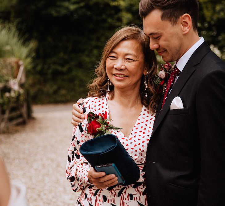 Mother of the Groom and The Groom in Black Moss Bros. Suit and Burgundy Tie Hugging