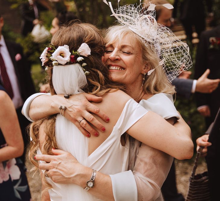 Mother of the Bride in a Birdcage Veil Hugging Her Daughter with Fresh Flowers in Her Hair