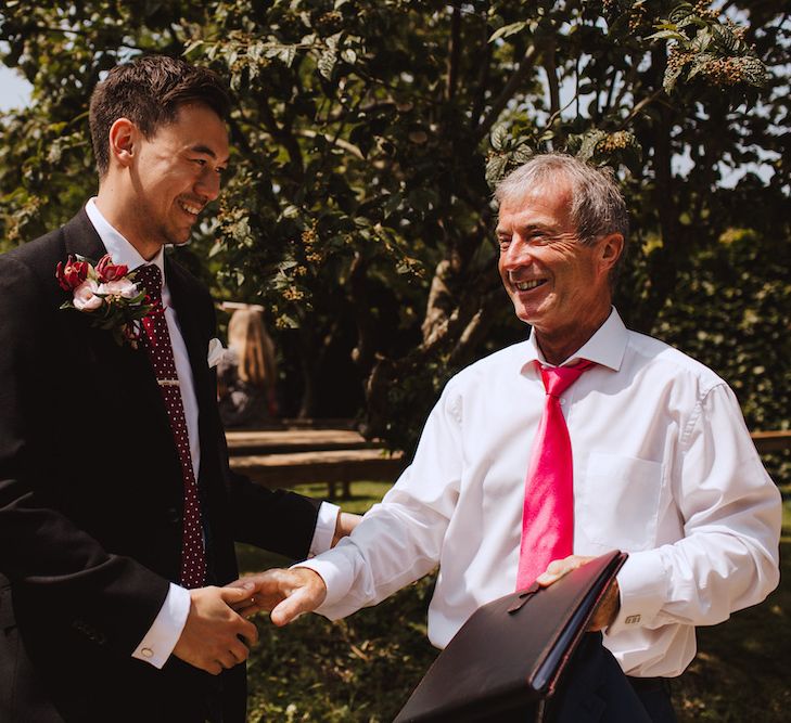 Groom in Moss Bros Suit &amp; Burgundy Tie Shaking Hands with a Wedding Guest