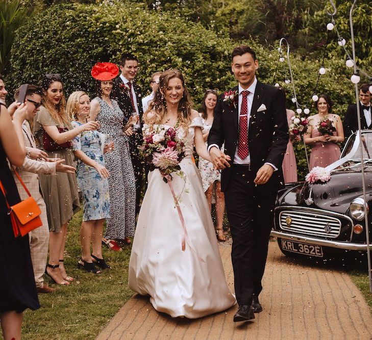 Confetti Moment with Bride in Bardot Wedding Dress and Groom in Black Moss Bros. Suit and Burgundy Tie