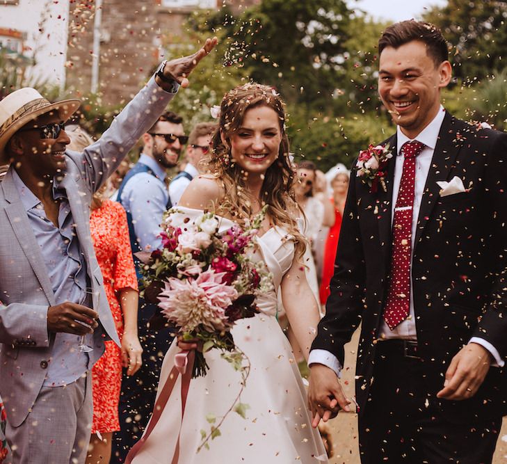 Confetti Exit with Bride in Bardot Wedding Dress and Groom in Black Moss Bros. Suit and Burgundy Tie