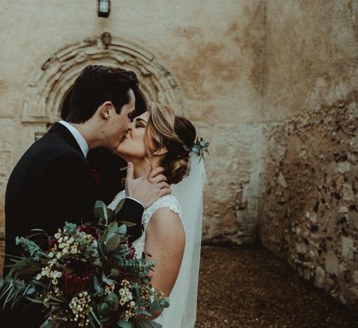 Bride in The Eleni Wed2B Lace Wedding Dress Holding a Protea Bridal Bouquet and Groom in Black Tie Kissing