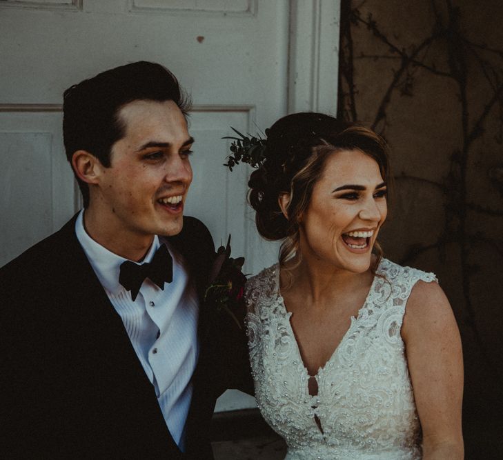 Bride in The Eleni Wed2B Lace Wedding Dress Holding a Protea Bridal Bouquet and Groom in Tuxedo Laughing