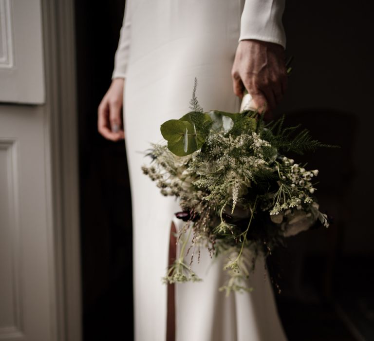 Bride in minimalist wedding dress holding a green and white bouquet