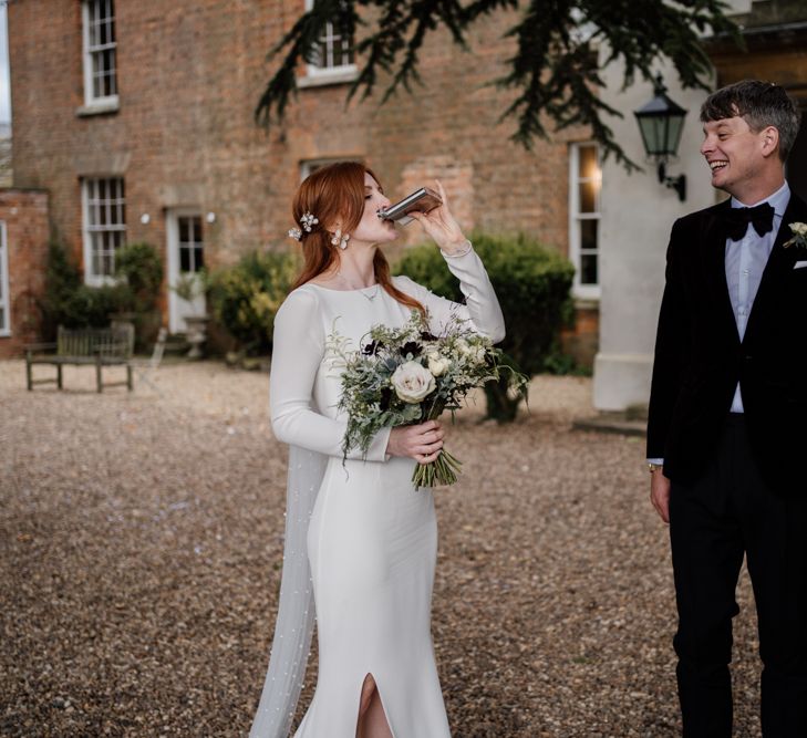 Bride in minimalist Alexandra Grecco wedding dress sipping from the grooms hip flask