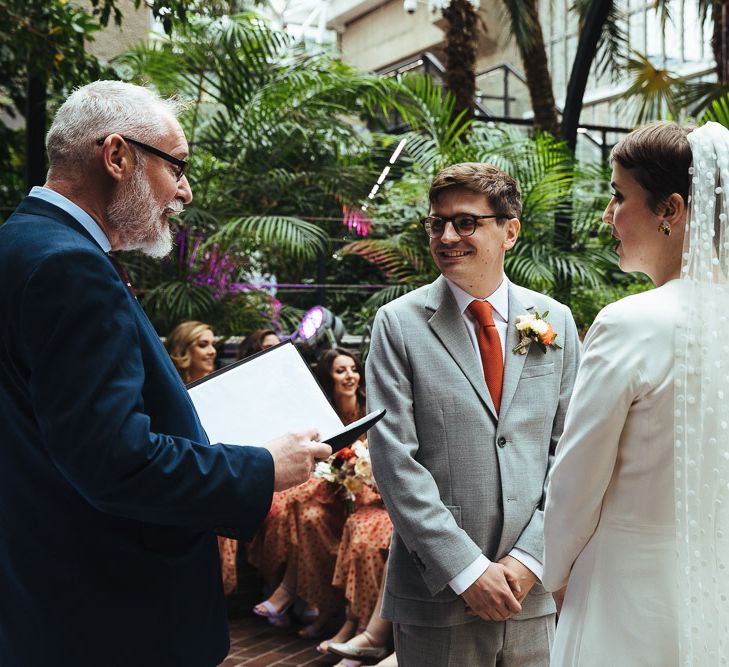 Groom in Grey Suit and Orange Tie and Bride in Cathedral Length Polka Dot Veil Standing at the Altar