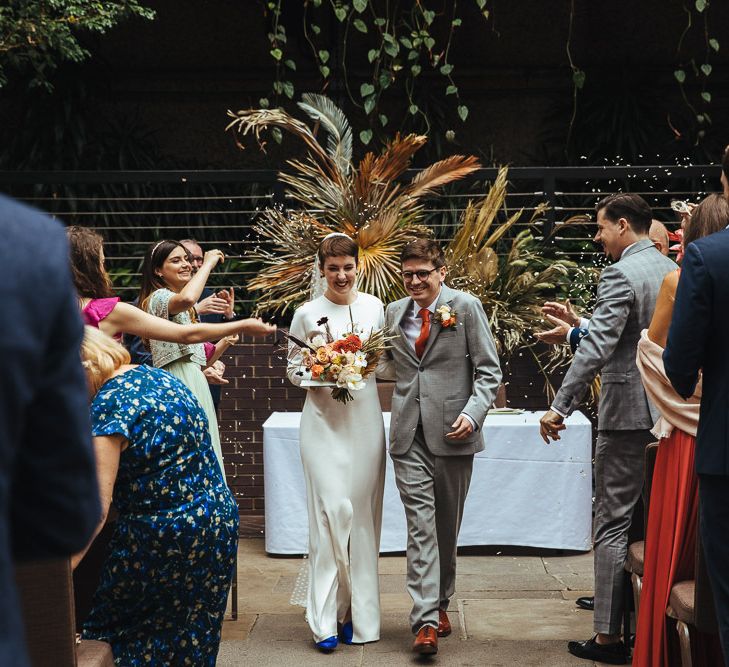 Bride in Minimalist Wedding Dress and Groom in Light Grey Suit Walking Up The Aisle as Husband &amp; Wife