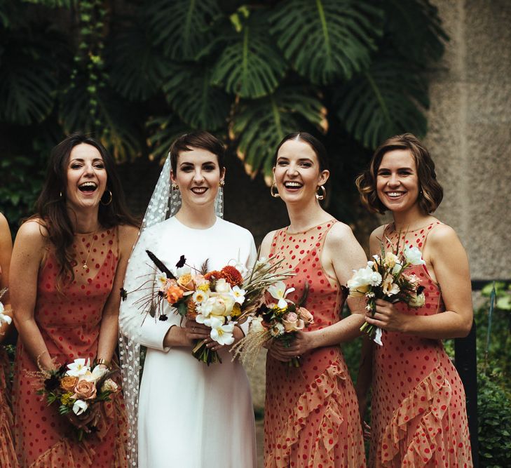 Bridal Party Portrait with Bridesmaids in Sheer Orange Polka Dot Dresses and Bride in Minimalist Charlie Brear Wedding Dress with Long Sleeves and Polka Dot Wedding Veil