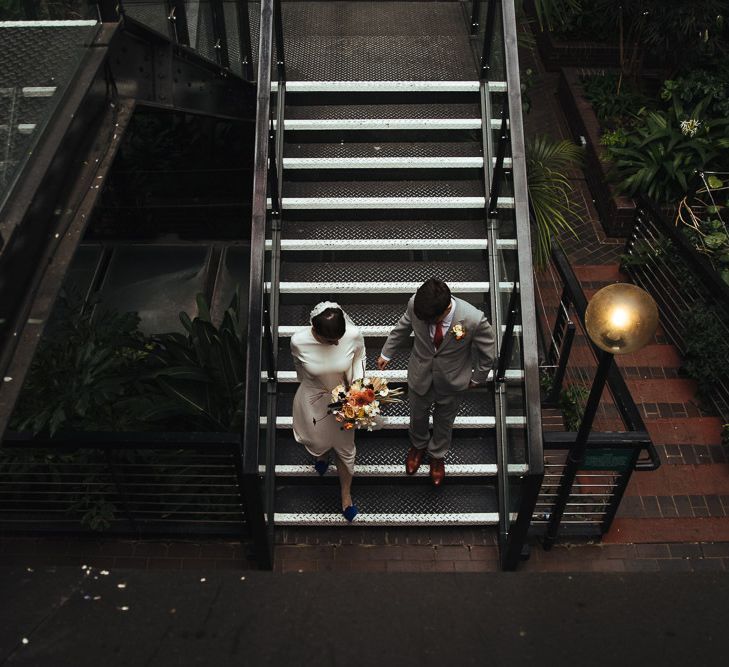 Bride in Charlie Brear Minimalist Wedding Dress and Groom in Grey Suit Walking Down the Stairs Together