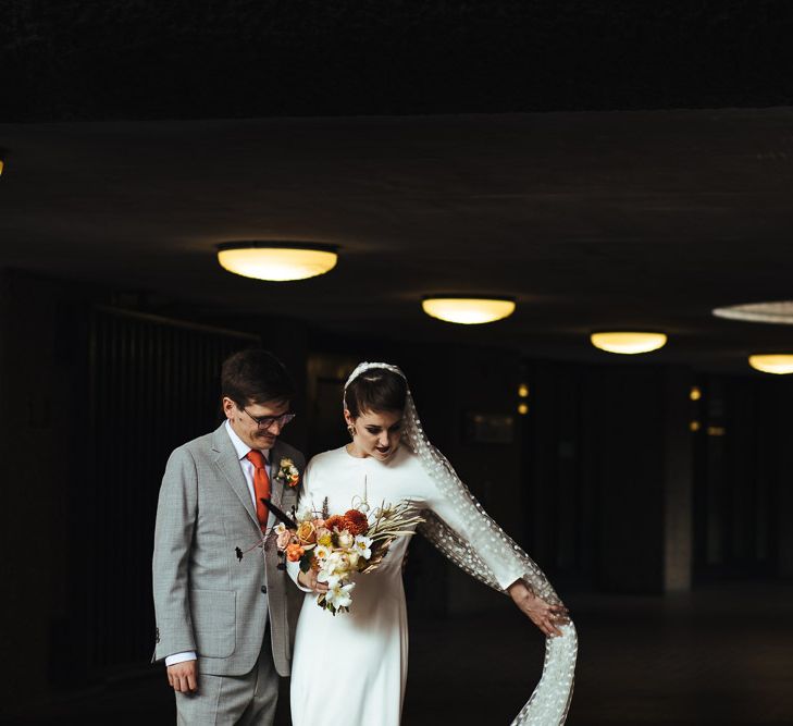 Bride in Charlie Brear Wedding Dress and Polka Dot Veil and Groom in Light Grey Suit