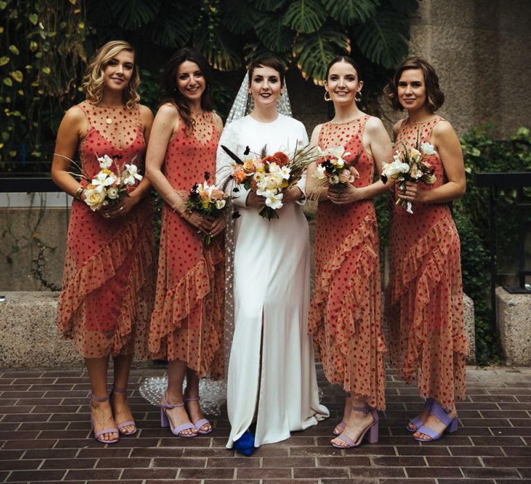 Bridal Party Portrait with Bridesmaids in Sheer Polka Dot Orange Dresses and Bride in Minimalist Charlie Brear Wedding Dress