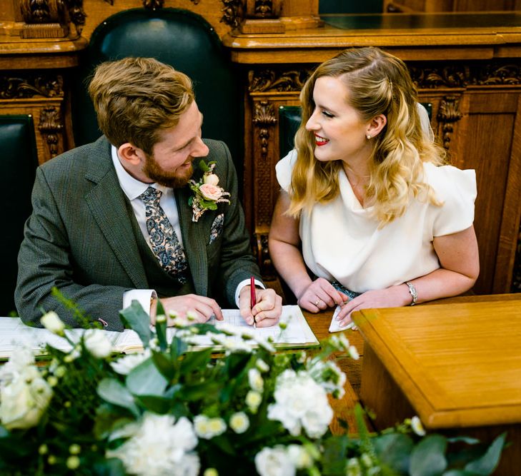 Bride in Vintage Wedding Dress and Groom in Tailored Suit Signing The Register