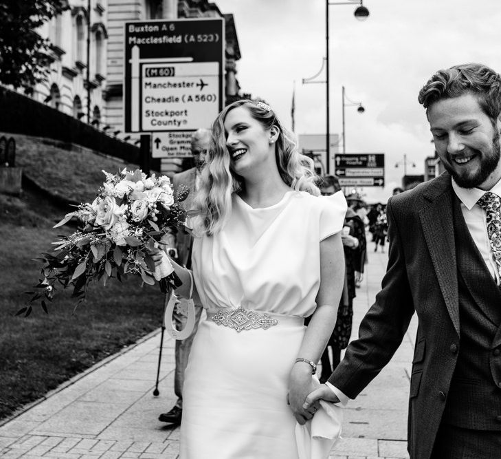 Black and White Portrait of Bride in Vintage Wedding Dress and Groom in Tailored Suit  Walking Through Manchester