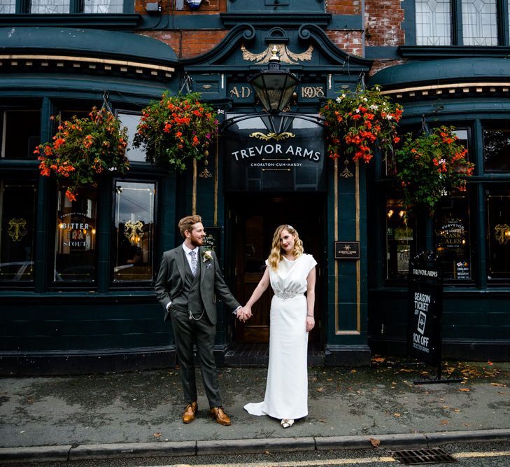 Bride with Satin Wedding Dress, Finger Waves and Red Lipstick, Holding Grooms Hand in Tailored Suit Outside Wedding Venue