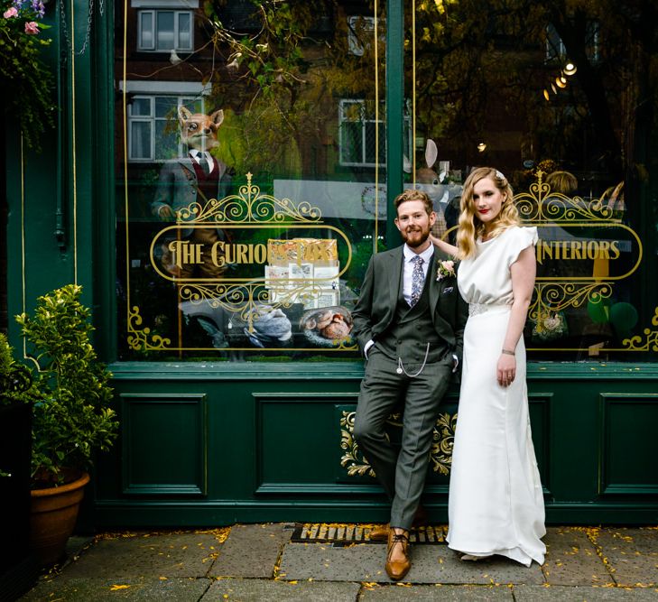 Vintage Bride Wearing a Satin Wedding Dress with Finger Waves and Red Lipstick, Standing with Groom in Tailored Suit Outside Wedding Venue