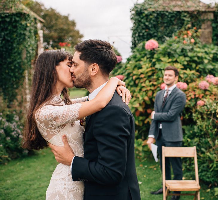 Bride in Catherine Deane Wedding Dress and Groom in Paul Smith Suit Kissing at the Altar