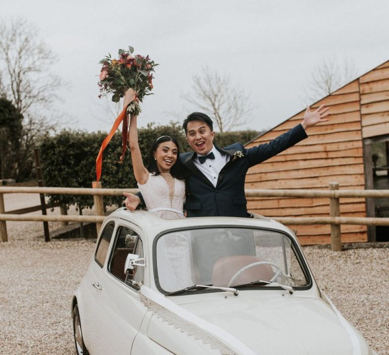 Bride and groom standing in the back of their convertible wedding car