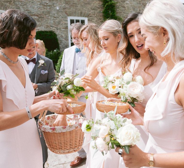 Bridesmaids in blush dresses take confetti from basket