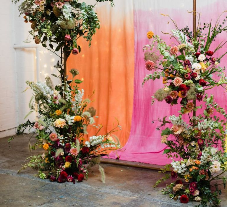 Hanging brightly coloured fabric backdrop with copper archway and floral decor