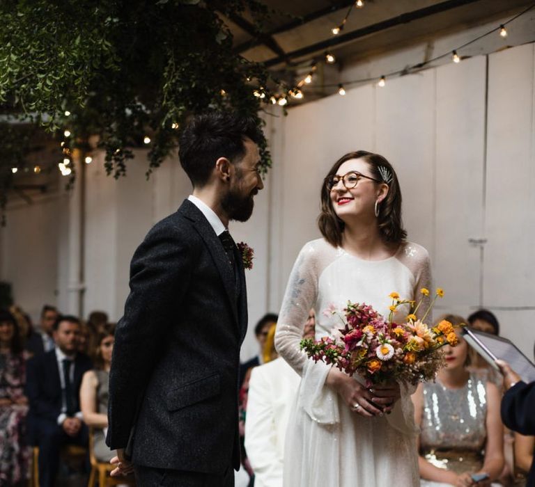 Bride in glasses wearing long sheer sleeved embellished dress and bright floral bouquet