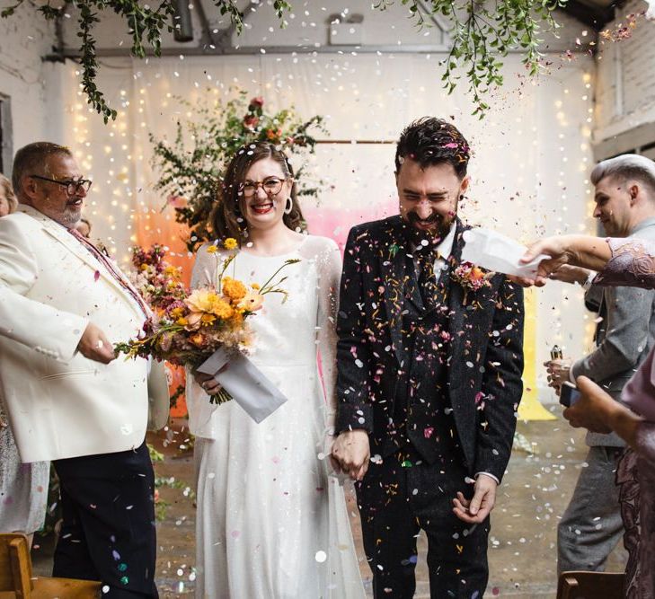 Bride in glasses confetti shot with bright floral bouquet and industrial styling