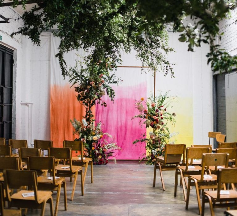 Copper arch with floral decor at industrial wedding ceremony with brightly coloured backdrop