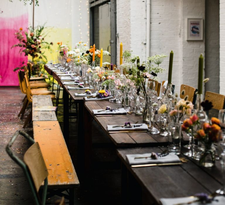 Table settings for industrial wedding reception in London with lots of bright floral decor and tall candlesticks