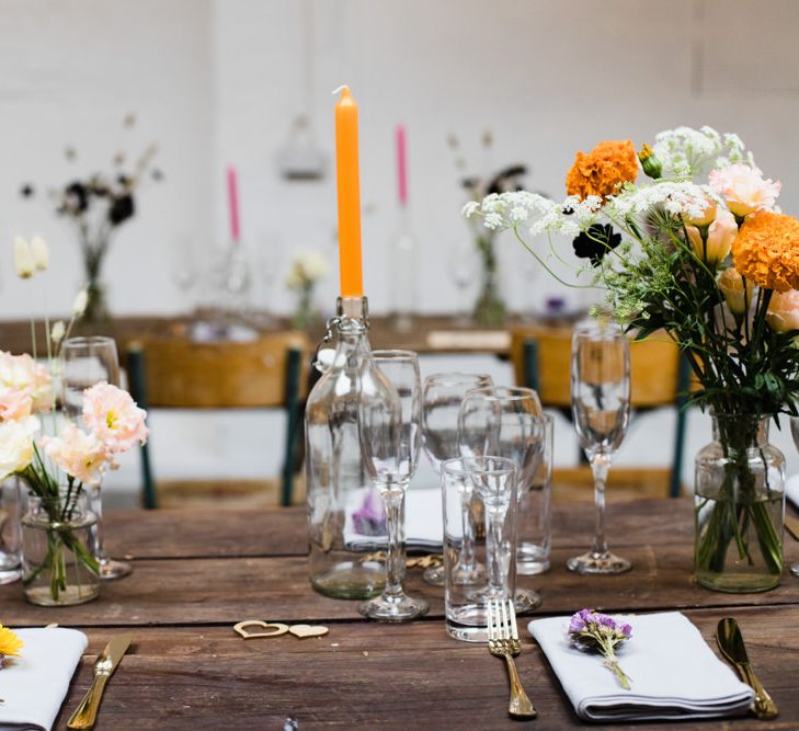 Table settings for industrial wedding reception in London with lots of bright floral decor and tall candlesticks