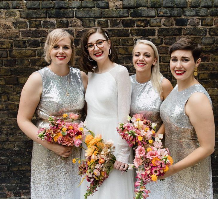 Bride in glasses with her bridesmaids wearing silver sequin dresses and brightly coloured bouquets