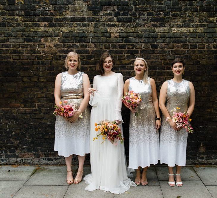 Bride in glasses and long sheer sleeve embellished dress with her bridesmaids wearing silver sequin dresses