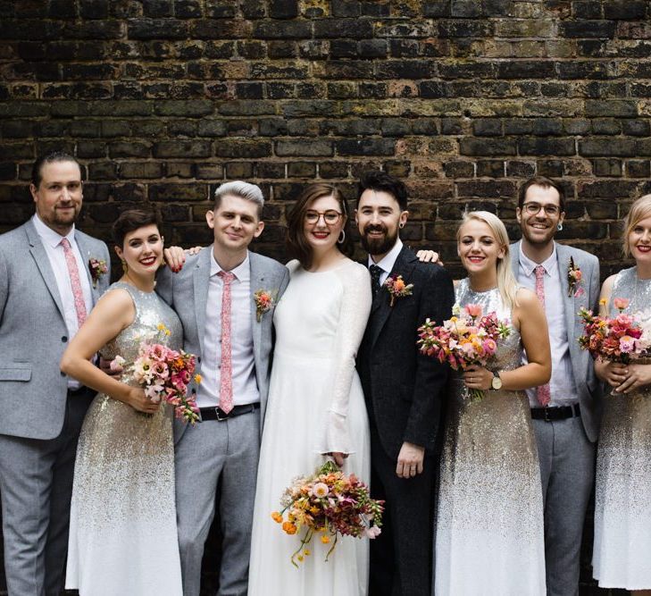 Bride in glasses with her groom and party at industrial wedding in London with bright floral bouquets and embellished dresses