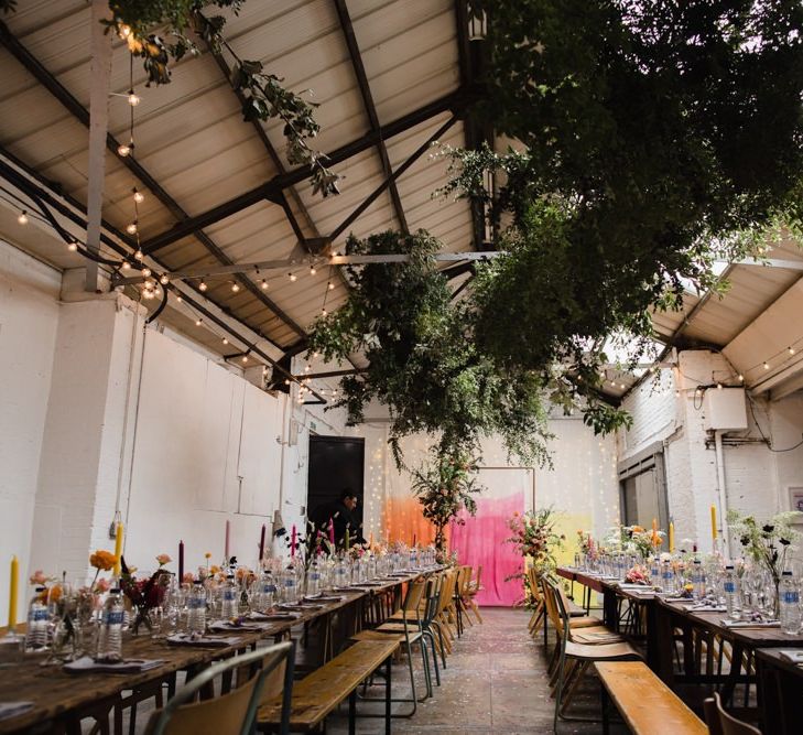 Industrial wedding reception in London with festoon lighting, hanging foliage and bright table decor