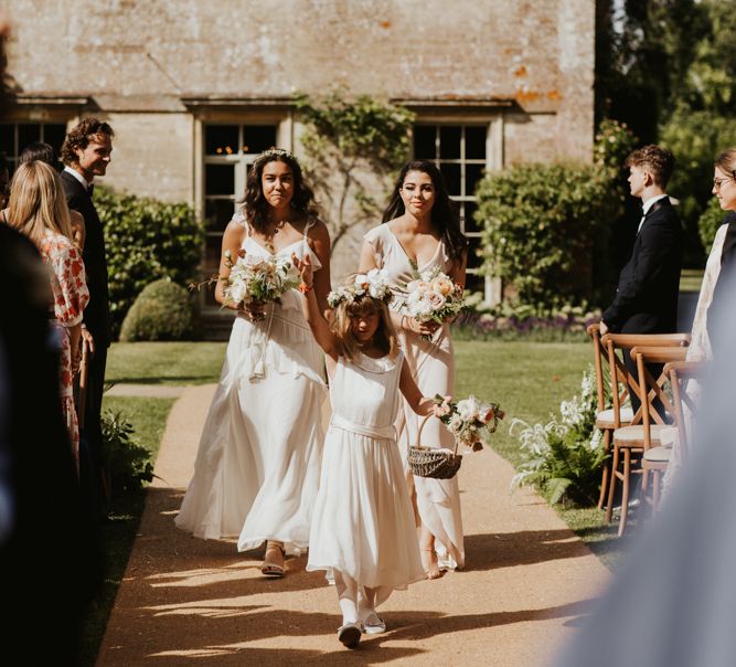 Flower girl and bridesmaids in white dresses walking down the aisle