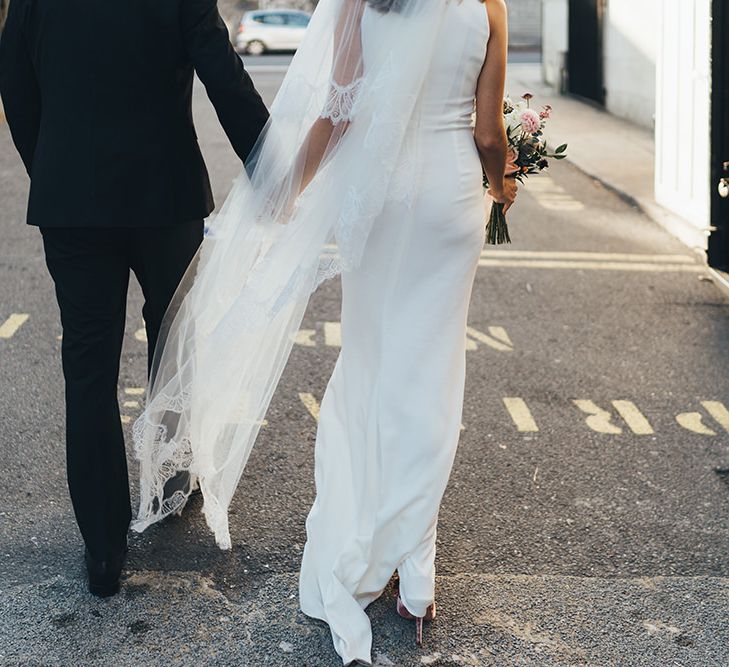 Back of Brides elegant dress with long veil walking through East London for autumn wedding celebration