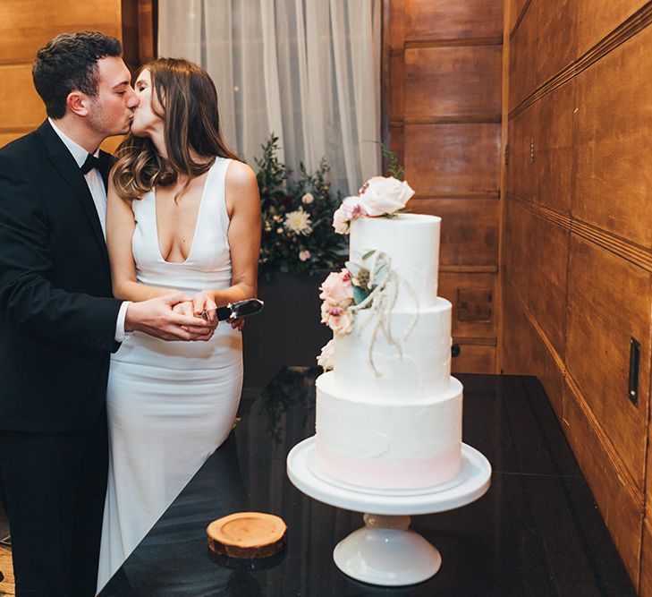 Bride and Groom cut into the white buttercream wedding cake with dusky pink floral decoration