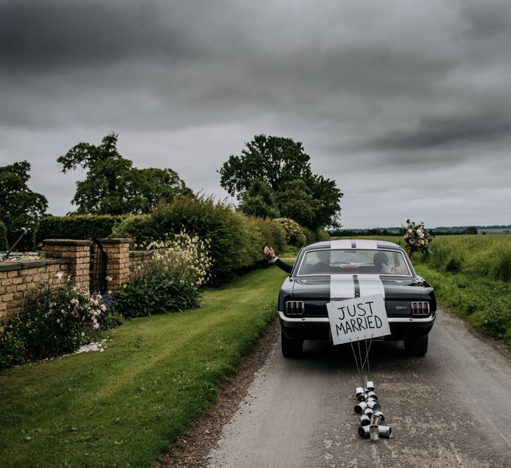 Bride and Groom Driving in a Black Ford Mustang Wedding Card with Just married Sign and Tin Cans Taped to the Back