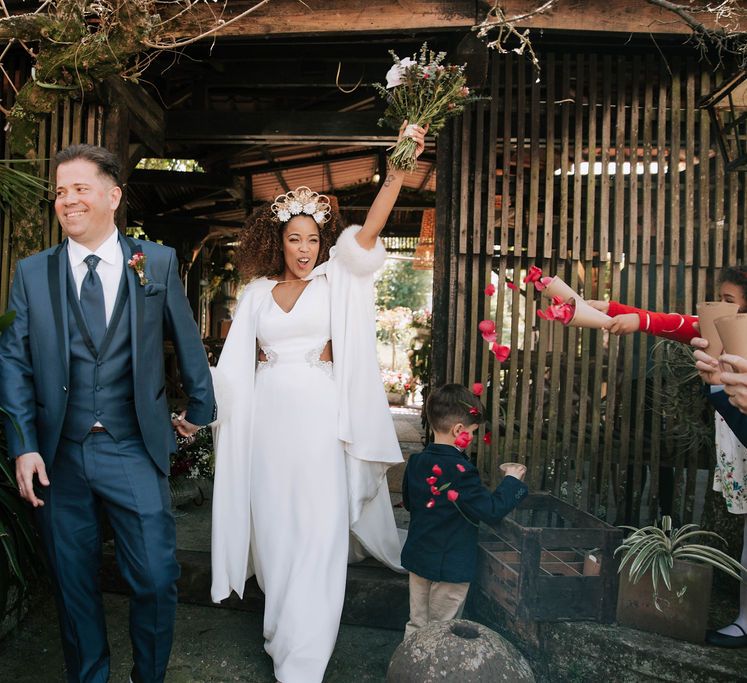 Bride with Afro Hair in Gold Headdress, Patricia Meléndez Wedding Dress and coat and Groom in Navy Suit Walking Out The Wedding Ceremony