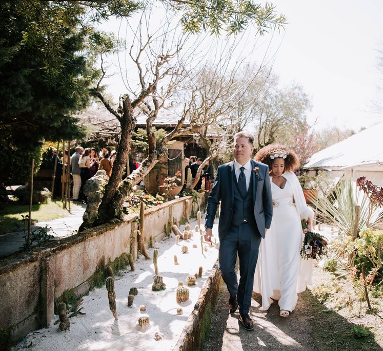 Bride with Afro Hair in Gold Headdress, Patricia Meléndez Wedding Dress and coat and Groom in Navy Suit Walking Through Fundación Sales Wedding Venue situated in the Galician south coast