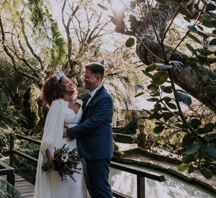 Bride in Patricia Meléndez Wedding Dress and Coat with blue fox wristband and Groom in Navy Suit Embracing