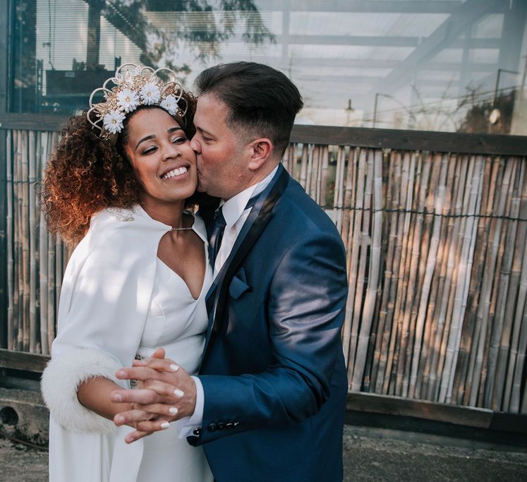 Groom in Navy Suit Kissing Bride with Afro Hair in Gold Headdress, Patricia Meléndez Wedding Dress and Coat