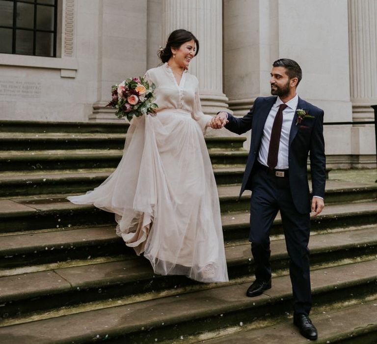 Groom helping his bride down the Old Marylebone Town Hall steps in her tulle skirt