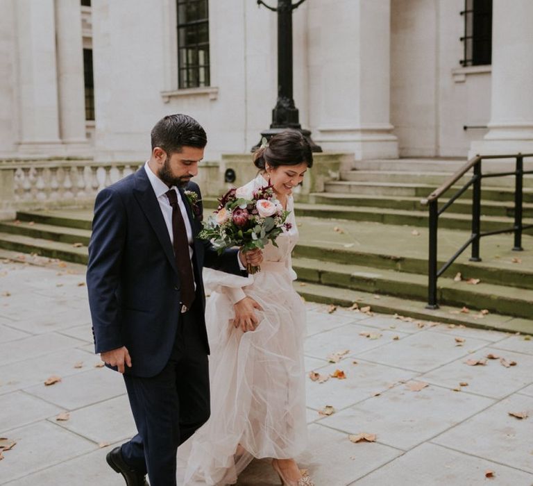 Bride and groom walking through London with autumn leaves on the floor