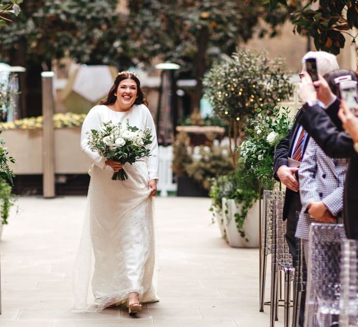 Bride walking down the aisle at courtyard ceremony with foliage decor