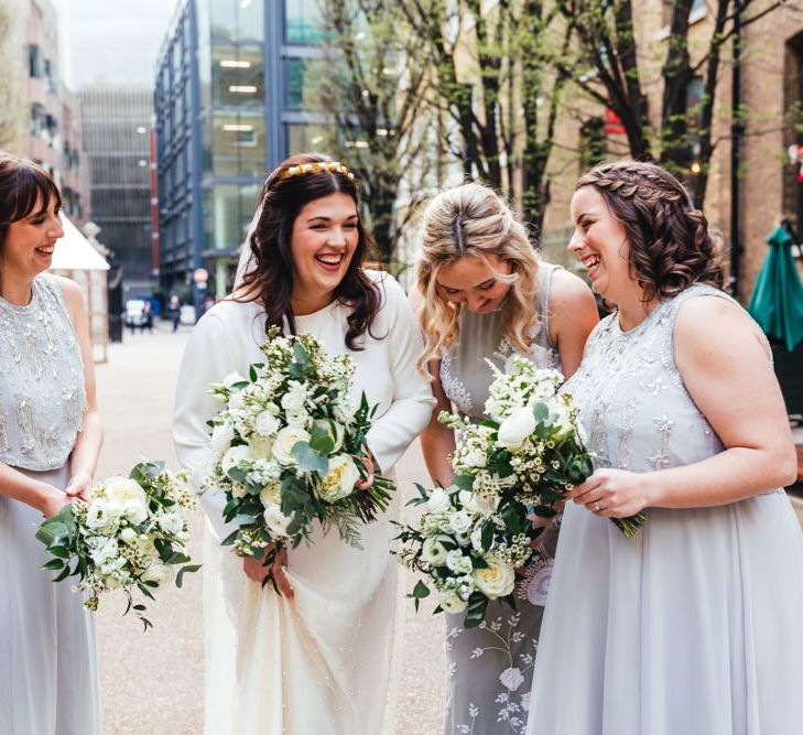 Bride and her bridesmaids wearing soft grey dresses and white floral bouquets