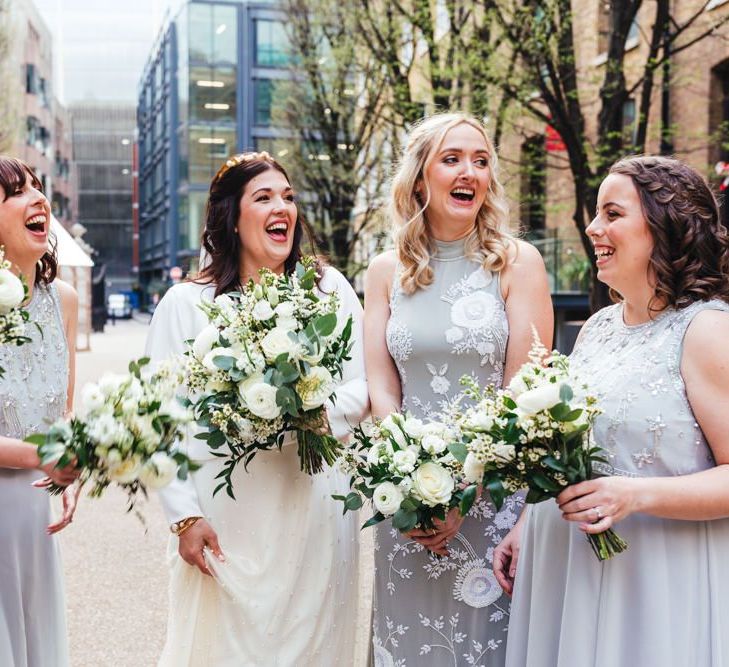 Bride and her bridesmaids wearing soft grey dresses and white floral bouquets