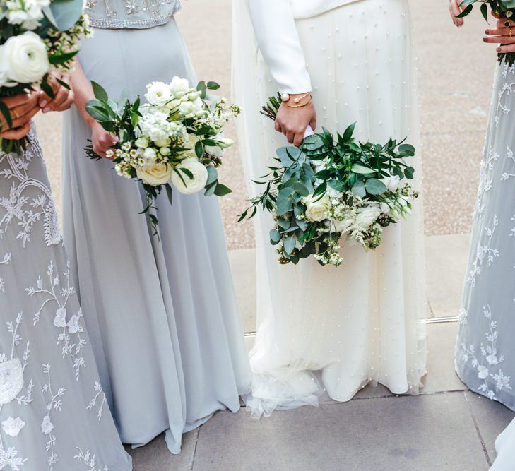 Bride and her bridesmaids wearing soft grey dresses and white floral bouquets