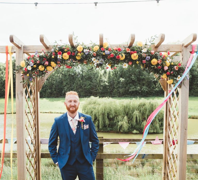 Groom at the Flower Covered Altar in Navy Suit | Bright Festival Themed Outdoor Ceremony &amp; Tipi Weeding |  Maryanne Weddings | Framed Beauty Film