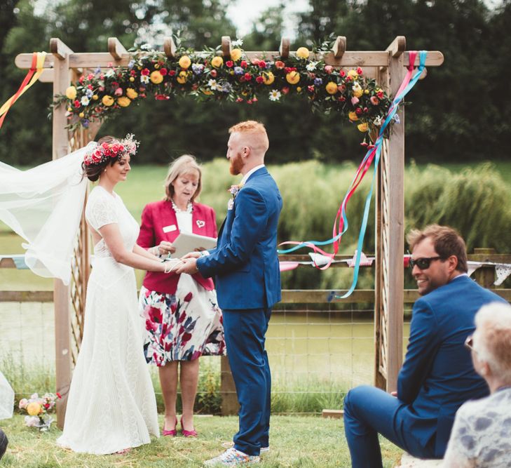 Wedding Ceremony | Bride in Lace Watters Gown &amp; Colourful Flower Crown | Groom in Navy Suit | Bright Festival Themed Outdoor Ceremony &amp; Tipi Weeding |  Maryanne Weddings | Framed Beauty Film