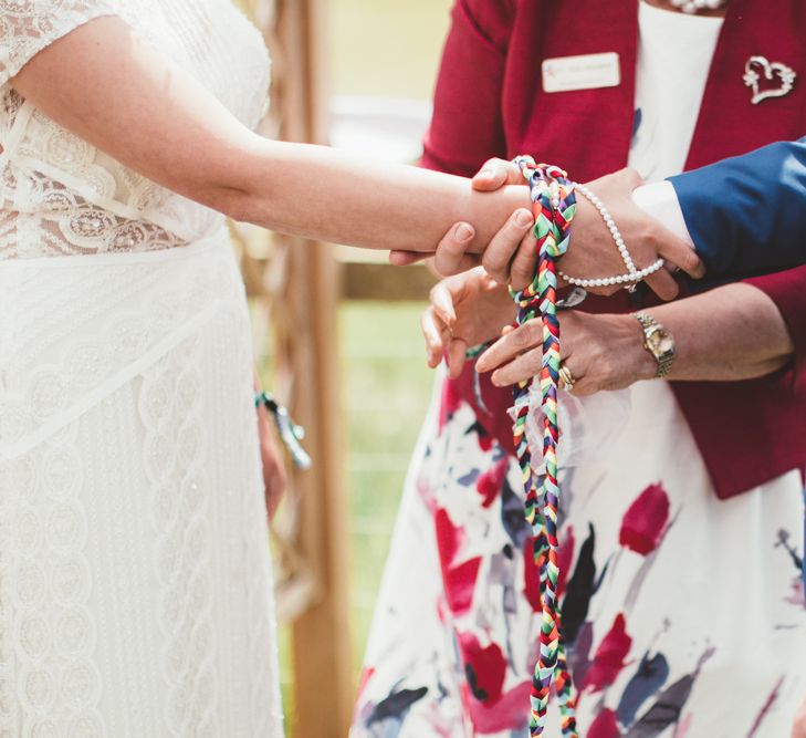 Hand Fastening Ceremony | Bride in Lace Watters Gown &amp; Colourful Flower Crown | Groom in Navy Suit | Bright Festival Themed Outdoor Ceremony &amp; Tipi Weeding |  Maryanne Weddings | Framed Beauty Film