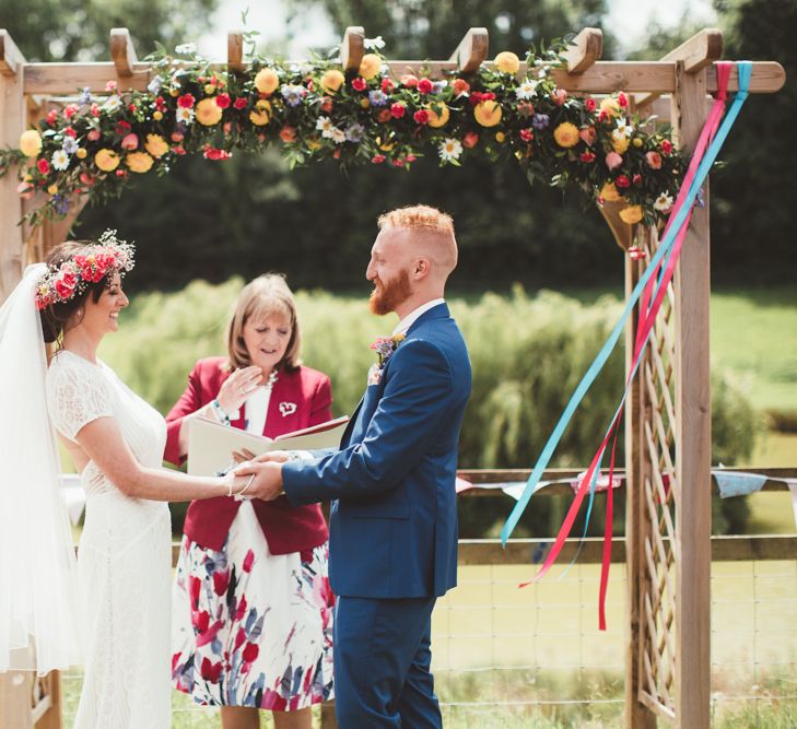 Wedding Ceremony | Bride in Lace Watters Gown &amp; Colourful Flower Crown | Groom in Navy Suit | Bright Festival Themed Outdoor Ceremony &amp; Tipi Weeding |  Maryanne Weddings | Framed Beauty Film